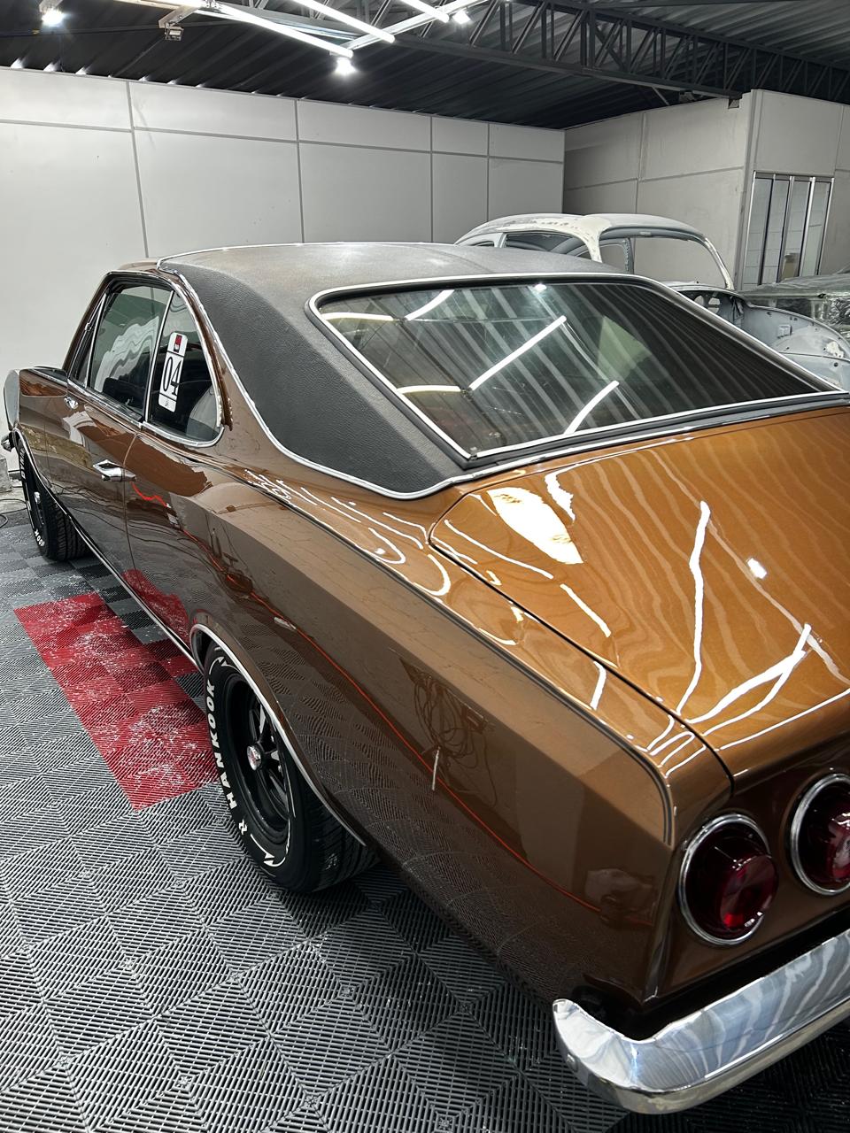 Traseira do Chevrolet Opala marrom antigo após polimento técnico, com Fuscas clássicos ao fundo